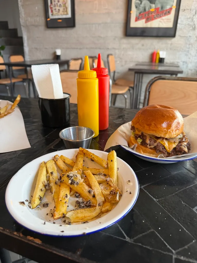 Plated burger and crispy fries on dark table with condiments