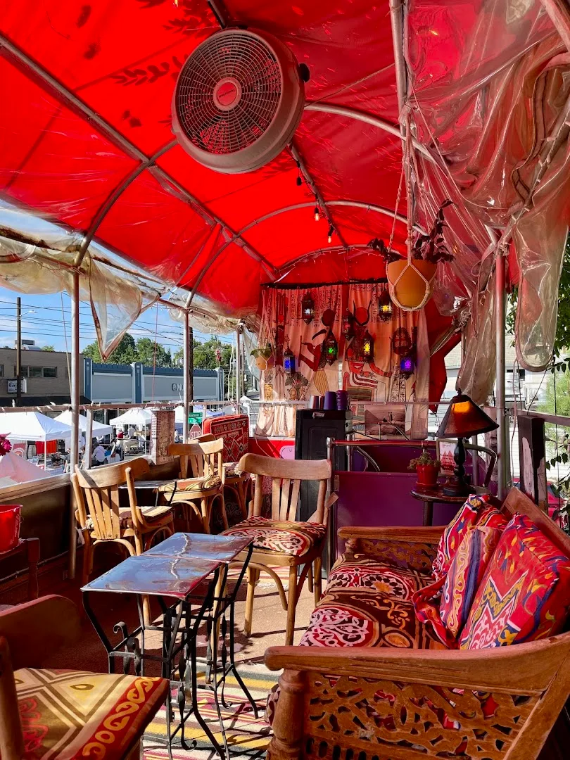 Red tent seating area with wooden chairs, cushions, overhead fan